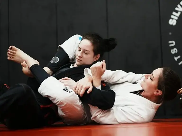 A high-contrast photo of two women practicing techniques during their self-defense lessons, with one athlete applying an armbar from the guard position.